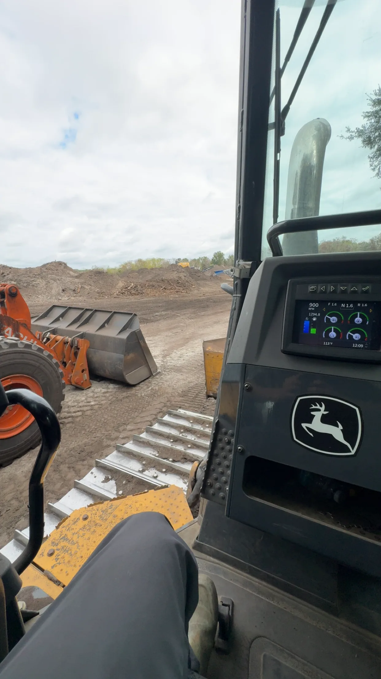 View from inside the cab of a John Deere dozer on a jobsite, wheel loader ahead